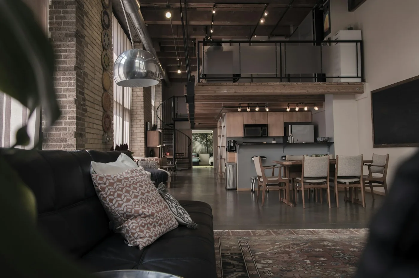 A loft apartment at rest: brick, steel and warm track lighting over a long dining table.
